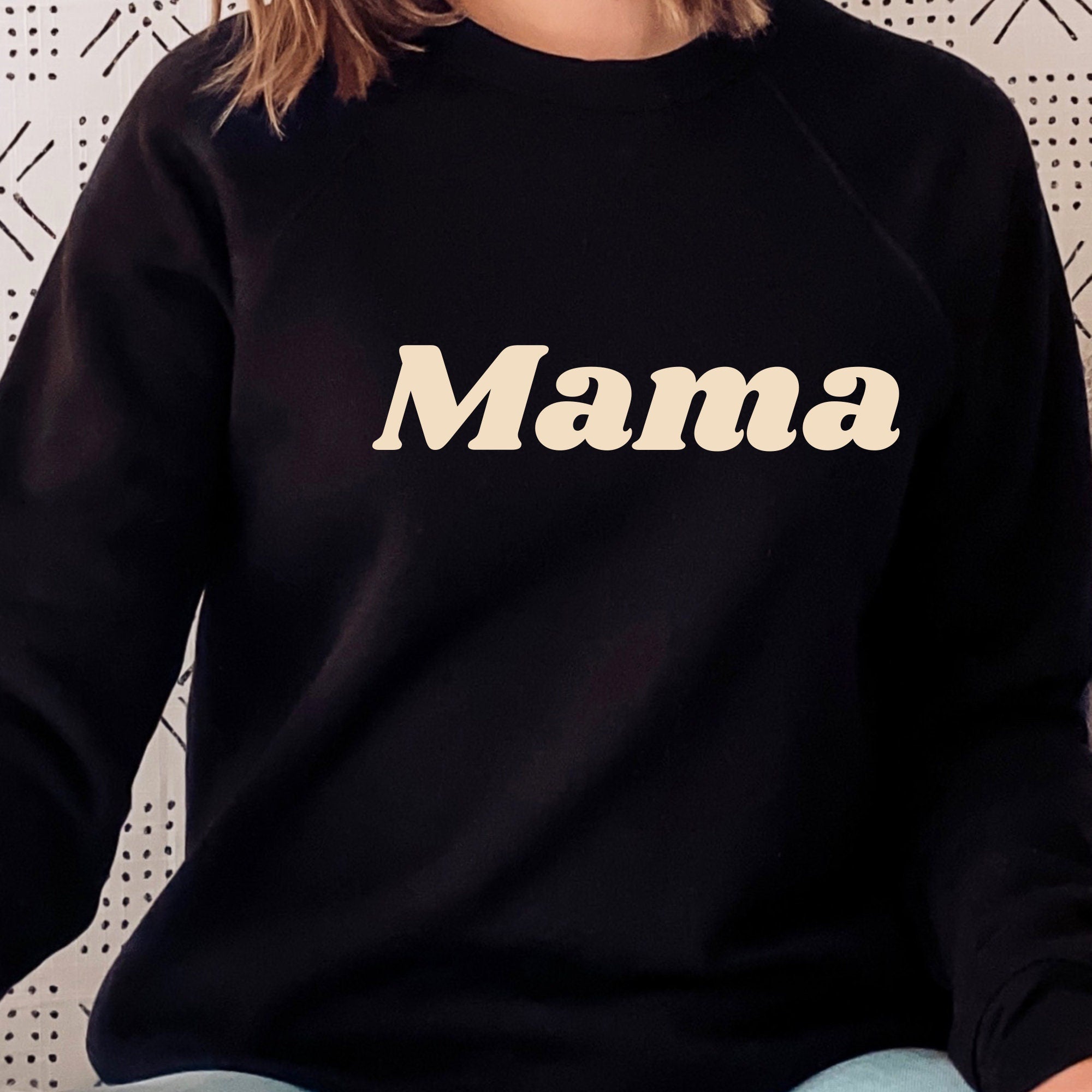 Black sweatshirt with 'Mama' printed on it against a neutral background