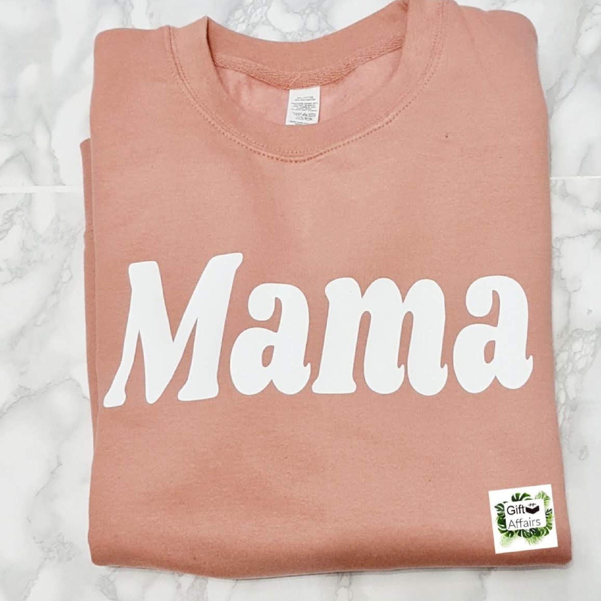 Folded pink sweatshirt with 'Mama' text on a marble surface