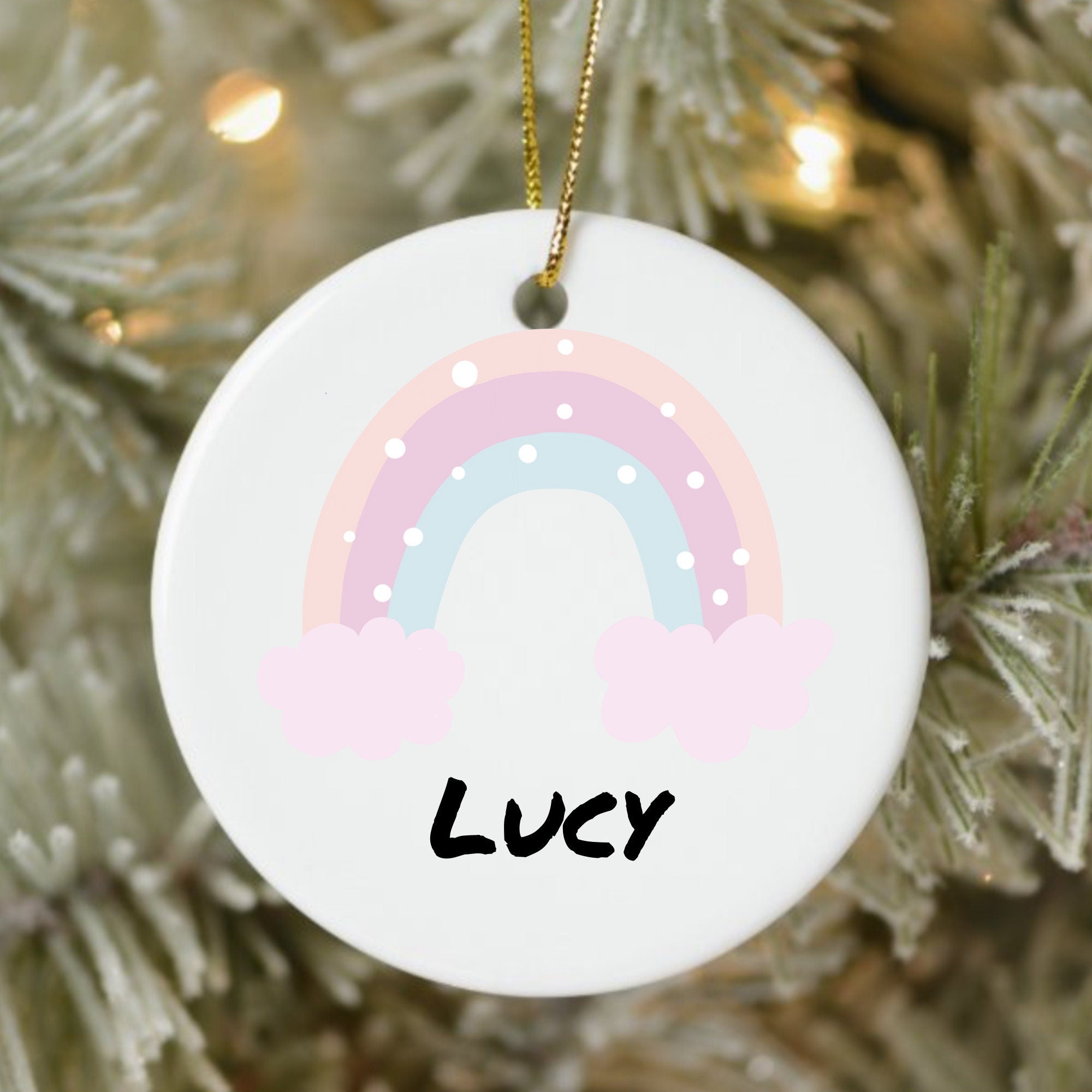 Round white ornament with a rainbow design and 'LUCY' text, hanging on a Christmas tree.