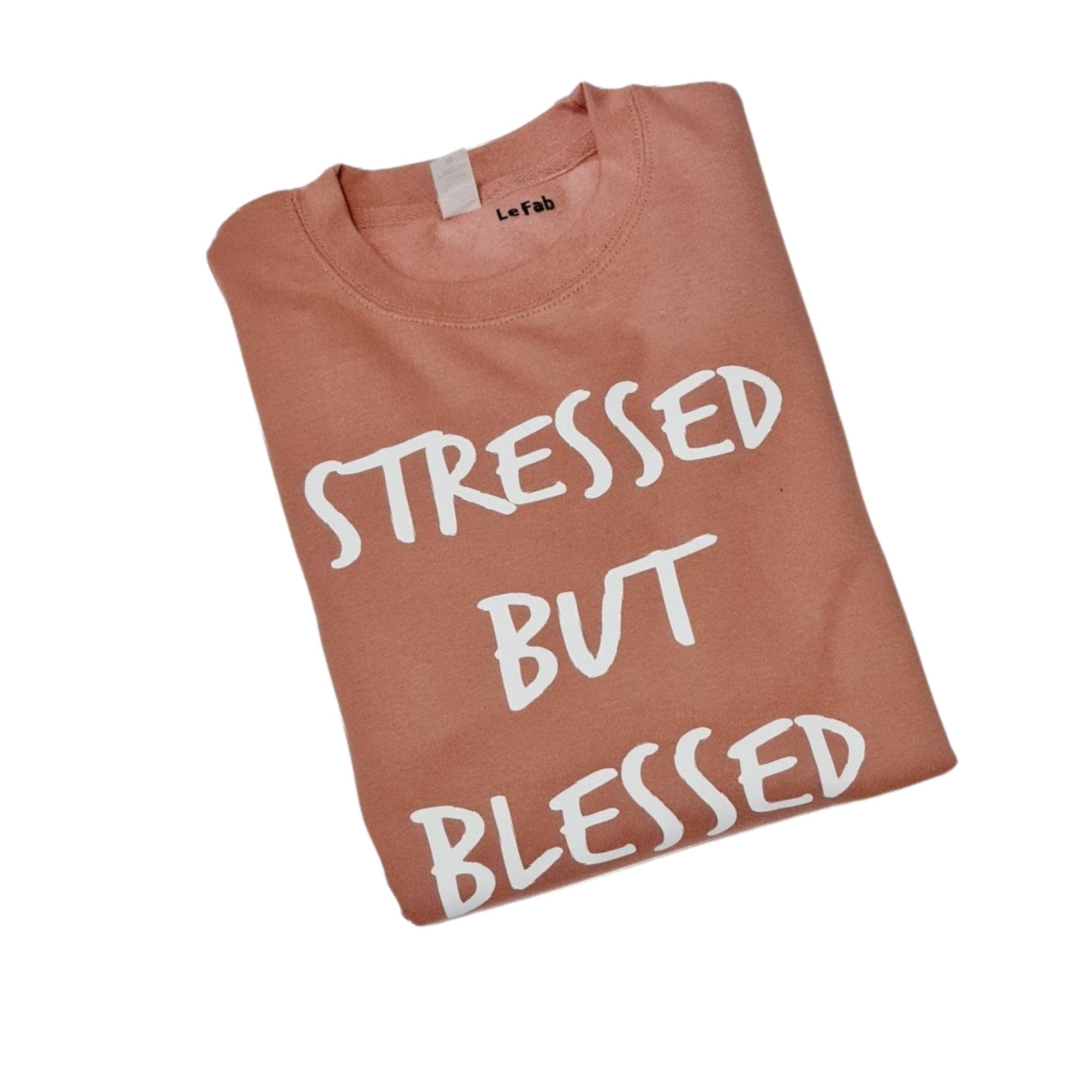 Folded pink t-shirt with 'STRESSED BUT BLESSED' text on a white background