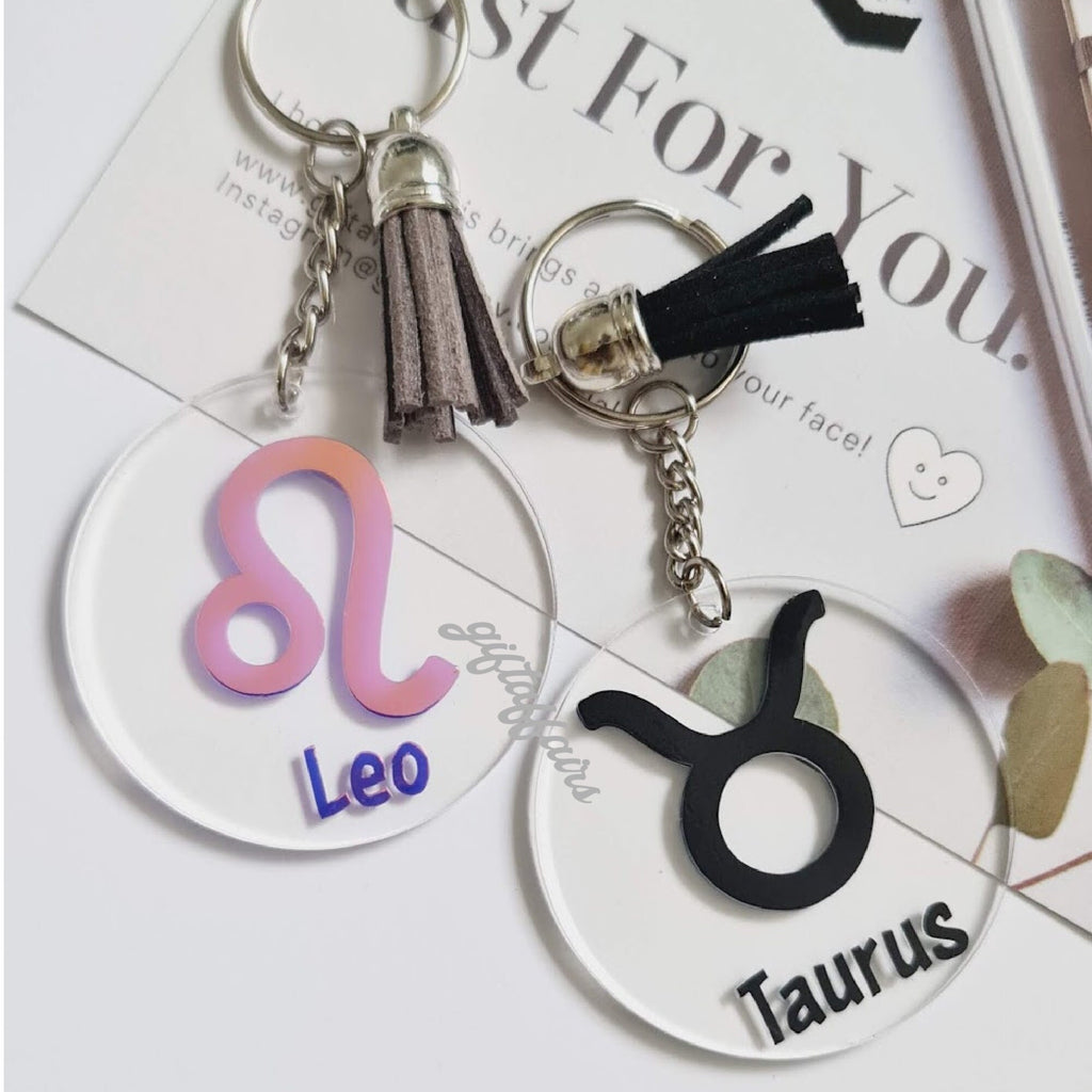 Two zodiac keychains, one for Leo and one for Taurus, on a magazine background.